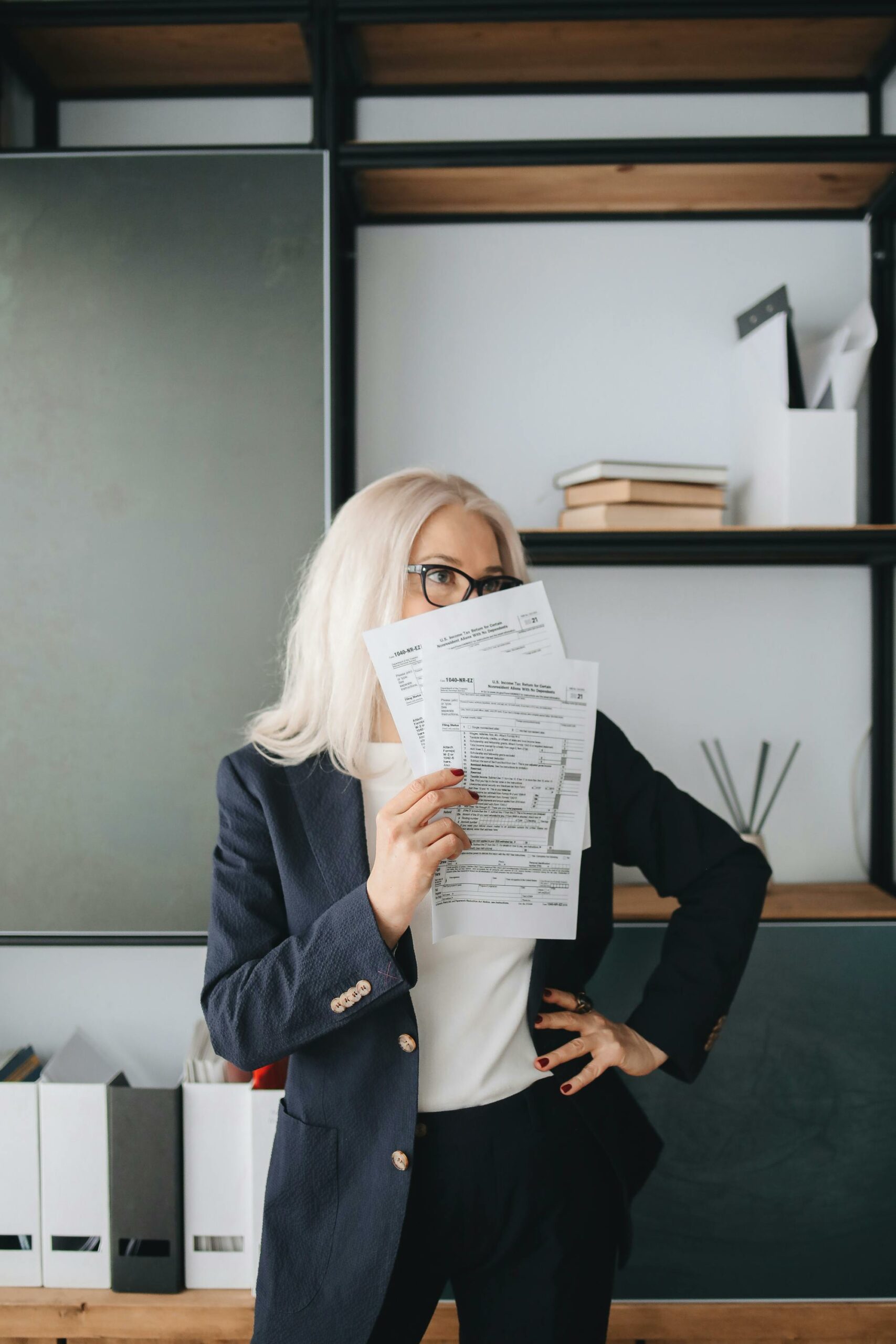 Businesswoman with glasses holding papers in a modern office setting.